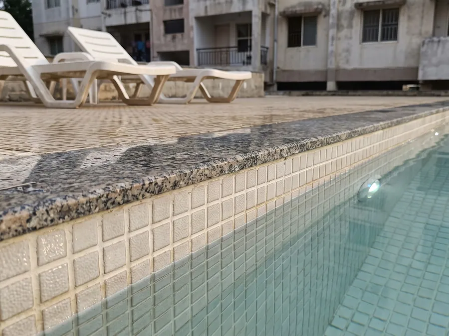The tiled waterline of an apartment swimming pool, mosaic joints crisp and evenly filled beneath the granite coping