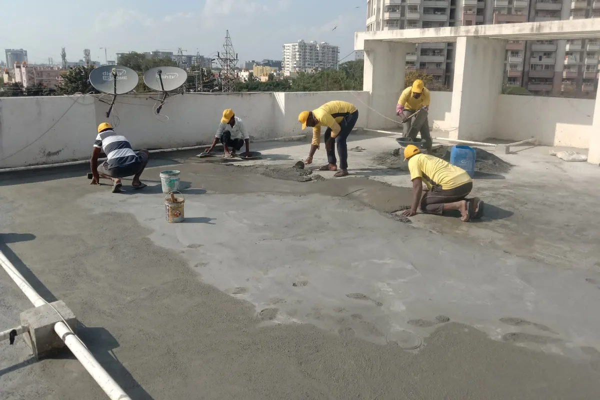 An Ultra Max crew troweling a fresh waterproofing coat flat across a Bengaluru terrace, apartment towers behind